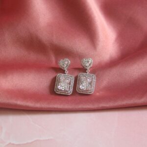 Pair of heart-shaped and rectangular diamond earrings displayed on a soft pink satin fabric.