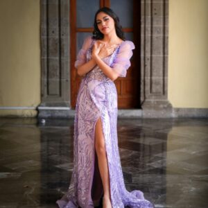 A woman in a purple gown poses gracefully indoors, exuding elegance in a historic setting.