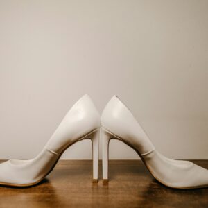Still life of elegant white high heel shoes placed on wooden table near wall